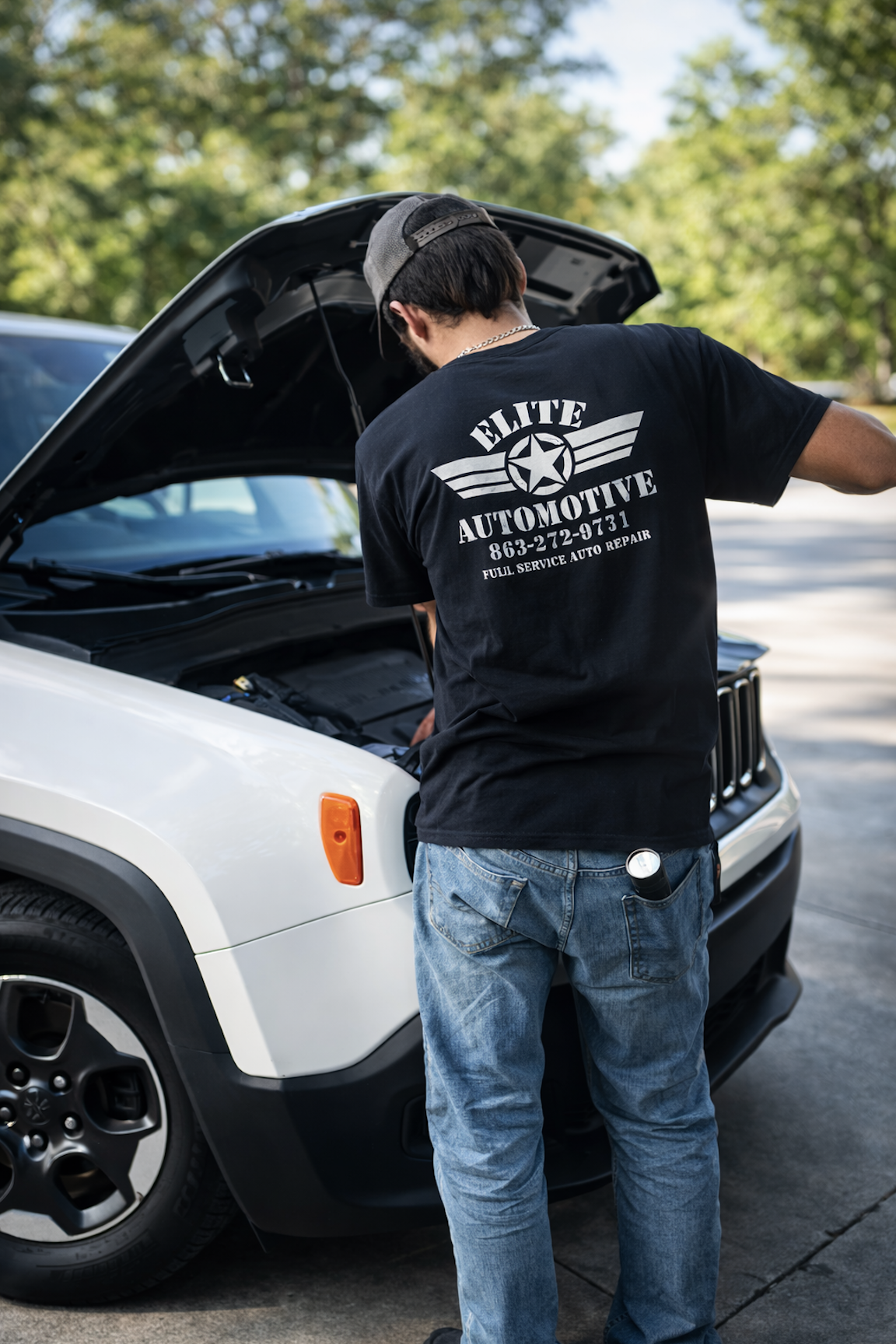Elite Automotive technician wearing branded shirt working under the hood of a white vehicle